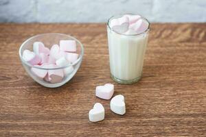 piatto trasparente con marshmallow a forma di cuore e un bicchiere di latte fresco sul tavolo. colazione. combinazione delicata foto