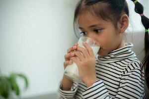 asiatico poco carino ragazzo Tenere un' tazza di latte nel il Casa. sentire contento e godere potabile latte. foto