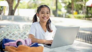 poco ragazza usi un' il computer portatile per imparare a scuola. il bambino sorrisi felicemente e prende conoscenza a distanza. foto