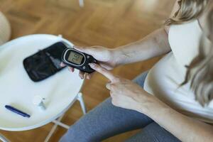 test sangue glucosio per diabete nel incinta donna con glucometro. uno rosso far cadere di sangue su il dito pronto per misurare zucchero livello. vicino su di maschio dito con sangue far cadere e test banda foto