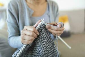 vicino su Visualizza nonna mani Tenere aghi rendere ripetitivo movimento maglieria seduta su divano la creazione di qualcosa con sua braccia. mano maglieria Ottimizzare cervello funzione, più vecchio generazione passatempo concetto foto