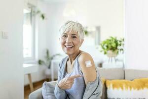 donna puntamento a sua braccio con un' bendare dopo ricevente il covid-19 vaccino. maturo donna mostrando sua spalla dopo ottenere coronavirus vaccino foto