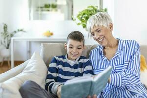 ritagliata foto di contento dai capelli grigi donna guardare a libro con sua nipote al chiuso. essi siamo sorridente durante loro conversazione. visitare nonni concetto