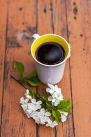 un' tazza di caffè su un' scuro, logoro rustico di legno tavolo. il composizione è decorato con un' ramoscello con bianca fiori. ciliegia albero fiori. selettivo messa a fuoco. foto