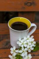 un' tazza di caffè su un' scuro, logoro rustico di legno tavolo. il composizione è decorato con un' ramoscello con bianca fiori. ciliegia albero fiori. selettivo messa a fuoco. foto