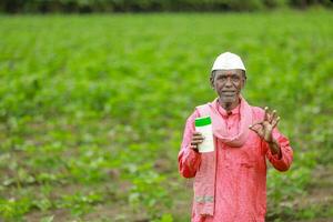 indiano contento contadino Tenere vuoto bottiglia nel mani, contento contadino mostrando bianca bottiglia foto