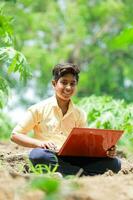 indiano ragazzo studiando nel azienda agricola, Tenere il computer portatile nel mano , povero indiano bambini foto