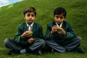 Due giovane ragazzi nel scuola uniformi godendo un' merenda nel il erba foto