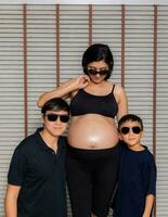 un' incinta madre vestito nel nero indossare bicchieri con sua marito e figlio. foto