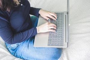 giovane donna seduta sul letto con il computer portatile in grembo.