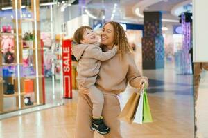contento e soddisfatto madre e poco ragazzo bambino con shopping borse nel il negozio. partire shopping con il bambini. foto