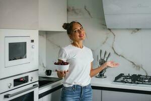 bella sorridente giovane donna detiene un' piatto di fresco ciliegia frutti di bosco nel sua mano nel il cucina foto