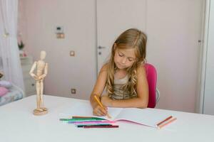 carino scolara bambino Sette anni vecchio è impegnato nel distanza apprendimento, disegno Lezioni, fare compiti a casa a casa foto