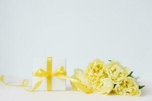 primavera composizione di un' mazzo di giallo tulipani, un' regalo con un' giallo arco e nastro su un' bianca sfondo. molla, Da donna giorno, di mamma giorno, compleanno. davanti Visualizza, copia spazio foto