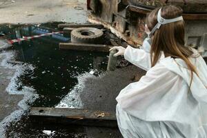 emergenza inquinamento fabbrica concetto. femmina chimico indossare ppe e gas maschera ispezionando olio su fabbrica pavimento foto
