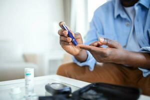 africano uomo è seduta a il divano a il casa e assunzione sangue a partire dal il suo dito dovuto per diabete. il quotidiano vita di un' uomo di afroamericano con un' cronico malattia chi è utilizzando glucosio tester. foto