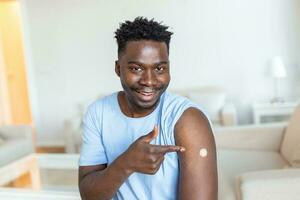 ritratto di un' uomo sorridente dopo ottenere un' vaccino. africano uomo Tenere giù il suo camicia manica e mostrando il suo braccio con bendare dopo ricevente vaccinazione. foto