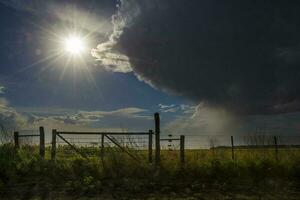 un' buio nube al di sopra di un' campo con un' recinto foto