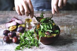 insalata sana mescolare le mani maschili con un cucchiaio e una forchetta. insalata di rucola e prugne. foto