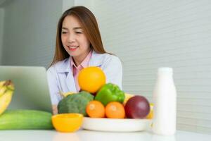 Ritratto di nutrizionista femminile sorridente asiatico che digita sul computer portatile per un programma di dieta correttiva equilibrata per consigli sul paziente o sulla perdita di peso. concetto di stile di vita sano, cibo sano, dieta foto