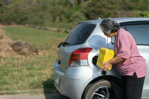 il auto corse su di gas e in stallo accanto il strada nel periferia e un anziano asiatico donna Usato un' gallone di scorta gas per carburante il macchina. un' donna prepara un' gallone di scorta gas per carburante prima in viaggio. foto