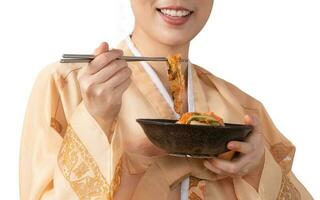 asiatico donne indossare coreano hanbok, Tenere kimchi ciotola e mangiare kimchi con un' bacchette. foto