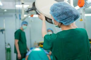 dietro a di asiatico chirurgo con un' medico maschera in piedi nel il operazione Teatro a un' Ospedale. squadra di professionale chirurghi. assistenza sanitaria, emergenza medico servizio concetto foto