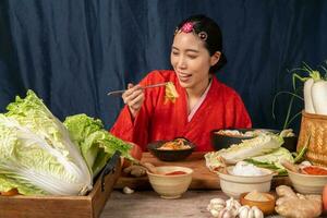 asiatico donne indossare coreano tradizionale costumi hanbok siamo miscelazione fresco saltato in padella e kimchi ingredienti con ingredienti come come sale, aglio, gochugaru, fresco verdure. foto