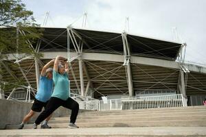 asiatico anziano coppie indossare gli sport attrezzatura e riscaldamento su muscoli prima esercizio a all'aperto nel il mattina. contento anziano all'aperto stile di vita concetto, pieno lunghezza di attivo contento anziano famiglia coppia foto