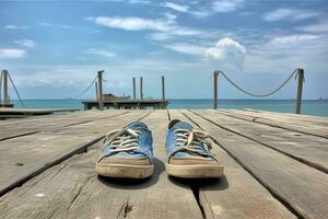 un' paio di blu e bianca scarpe seduta solo su un' di legno passerella vicino il oceano. il scarpe siamo posizionato nel il primo piano, con il sereno mare e bacino nel il sfondo. foto