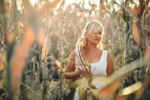 donna in un abito lungo estivo bianco cammina su un campo di grano e posa nell'ora del tramonto.