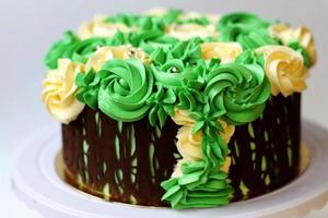 splendida torta fatta in casa ricoperta di rose gialle e verdi fatta di crema al burro, cornice di cioccolato, glassa su sfondo bianco foto