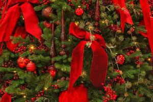 avvicinamento di Natale albero nel il Casa con decorazione. ghirlanda, luci, palline, Rowan e nastro fiocchi su abete rosso abete rami. inverno vacanze composizione foto