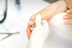 il manicure detiene il femmina pollice durante un' manicure procedura nel il chiodo salone. foto