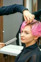 femmina parrucchiere messa in piega corto rosa capelli di il giovane bianca donna con mani e pettine nel un' capelli salone. foto