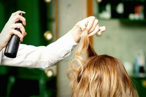 femmina coiffeur fissaggio stile di capelli di bionda donna con lacca per capelli nel un' bellezza salone. foto