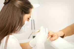 manicure maestro nel protettivo viso maschera e bianca guanti applicare polacco per femmina unghie. foto