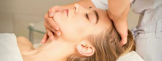 cosmetologo mani fare facciale massaggio su fronte e mento di giovane femmina a terme salone. foto