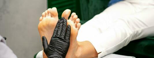 idratante il piedi. mani di pedicure maestro nel nero guanti cura di femmina piedi. piede massaggio. pedicure bellezza salone concetto. foto