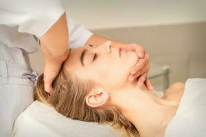 cosmetologo mani fare facciale massaggio su fronte e mento di giovane femmina a terme salone. foto