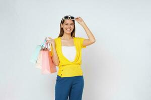 ritratto di eccitato emotivo giovane donna indossare e toccante occhiali da sole Tenere colorato shopping borse isolato su bianca sfondo. foto
