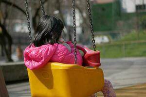 bambino avendo divertimento su un' swing su il terreno di gioco nel pubblico parco. foto