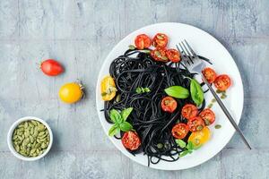 pronto per mangiare nero spaghetti con secco pomodori, sesamo semi e zucca su un' piatto su il tavolo. buongustaio cibo. superiore Visualizza. copia spazio foto