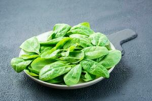 un bracciata di fresco bambino spinaci le foglie nel gocce di acqua su un' piatto su un' ardesia tavola. vegetariano, benessere e disintossicazione cibo foto