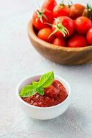 pomodoro incolla e basilico le foglie nel un' ciotola e pomodori su un' piatto su un' leggero sfondo. verdura e vegetariano cibo. vitamine e disintossicazione dieta. verticale Visualizza foto