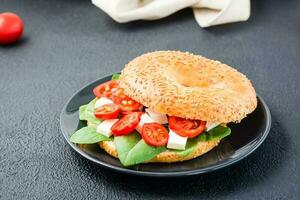 appetitoso pronto a mangiare bagel ripieno con pomodori, feta e spinaci le foglie su un' piatto su un' nero sfondo. leggero salutare merenda foto