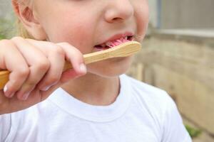 un' bambino spazzole il suo denti con un' di legno spazzolino. foto