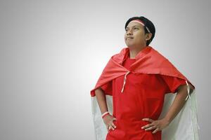 ritratto di attraente asiatico uomo nel maglietta con rosso bianca nastro su testa con bandiera su il suo spalla come un' mantello, guardare su con mani su anca. isolato Immagine su grigio foto