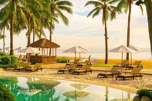 bellissimo ombrellone di lusso e sedia intorno alla piscina all'aperto in hotel e resort con palme da cocco al tramonto o all'alba sky foto