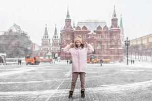 una bella ragazza con una giacca rosa cammina lungo piazza manezhnaya a mosca durante una nevicata e una bufera di neve. gli spazzaneve stanno lavorando in background.